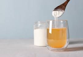 colageno hidrolizado en un frasco, vaso con agua para preparar colageno bebible, y una cuchara vertiendo el polvo